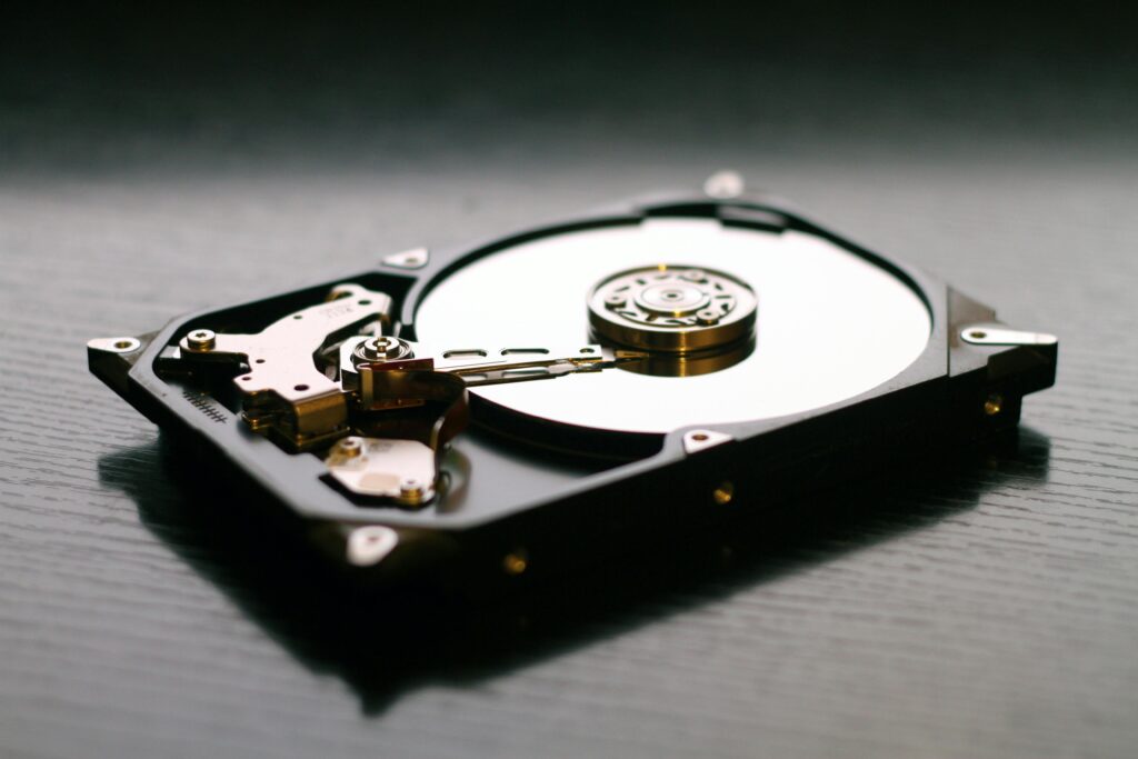 An open hard drive is displayed on a wooden surface, showcasing its internal components and metallic details.