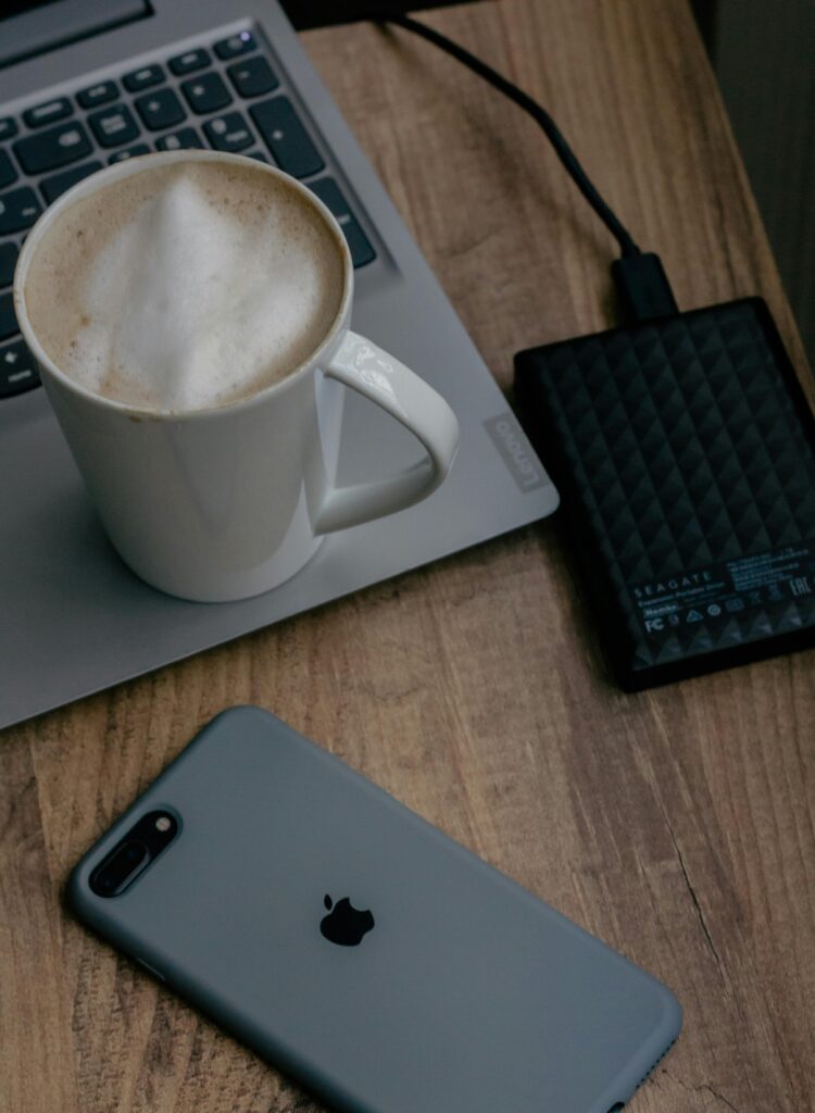 Cozy workspace with laptop, phone, coffee, and external hard drive on wooden table.