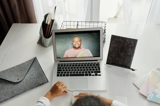 A student participates in a virtual class with a teacher on a laptop screen.