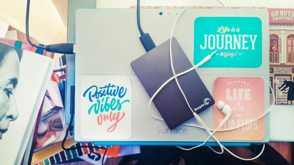 Top view of a laptop with motivational stickers, an external hard drive, and earphones on a colorful desk.