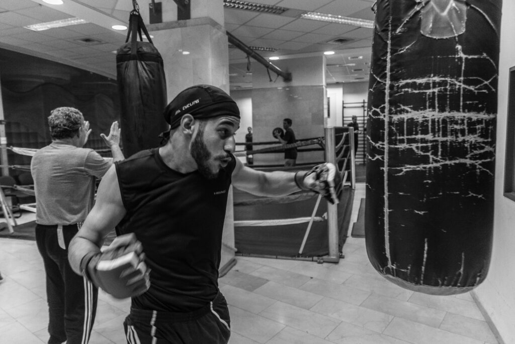 A young male boxer training with a punching bag in a gym, showcasing technique and power.