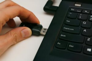 Close-up of a USB pen drive being inserted into a laptop USB port on a white surface.