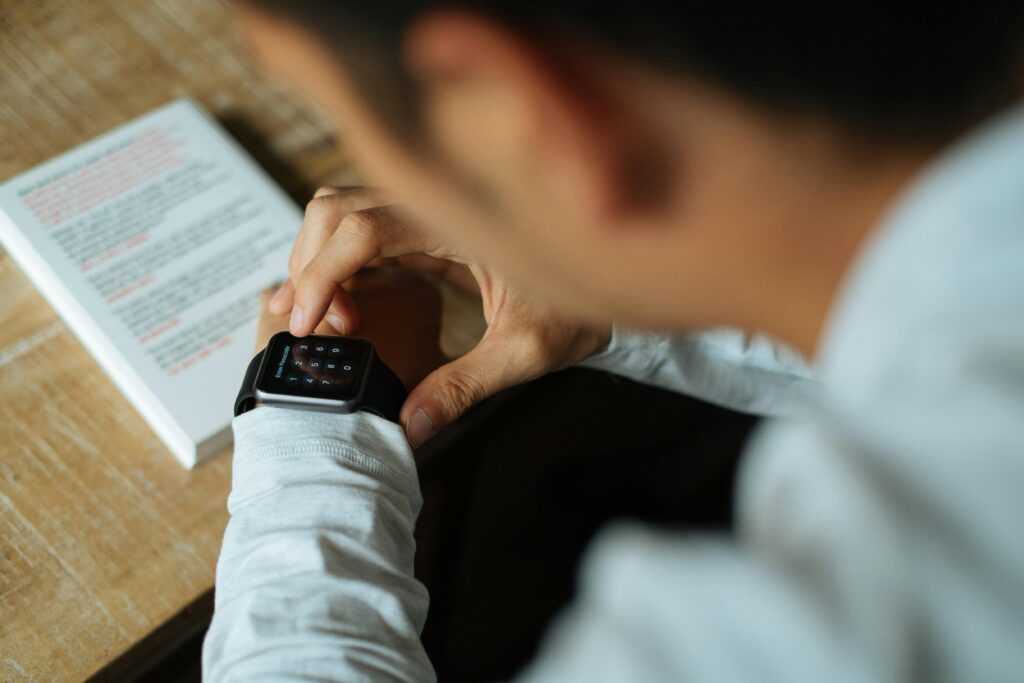 A man interacts with a smartwatch while sitting indoors, focusing on technology and multitasking.