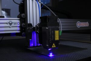 Close-up of a high-tech laser cutter operating indoors with blue lighting.