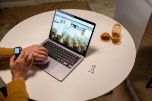 Person in yellow sweater working at a laptop with a smartwatch, AirPods and a modern workspace setup.