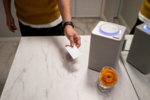 A person interacts with a smart speaker on a marble table, showcasing contemporary technology use.