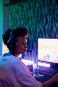 Teenage boy engaged in online gaming with headphones in a dimly lit room.